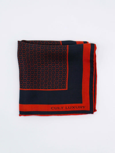 Red and black silk pocket square from Cult Luxury, folded to highlight the intricate CL monogram design and bold contrasting border