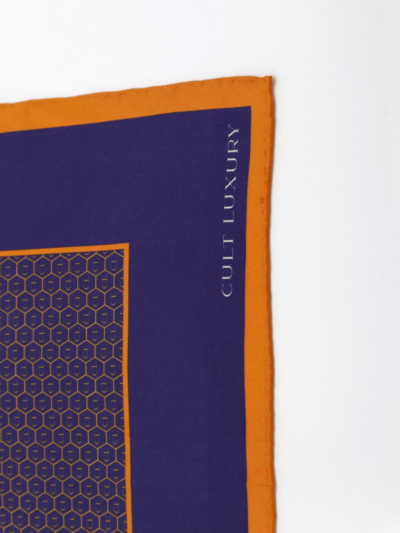 Close-up detail of the Cult Luxury royal blue silk pocket square, featuring intricate monogram design and vibrant orange border.