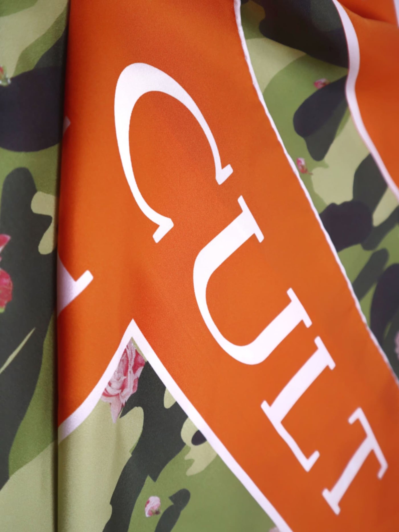 Detailed close-up of the luxurious silk twill scarf, highlighting the vivid orange “Cult Luxury” typography and floral camouflage design.