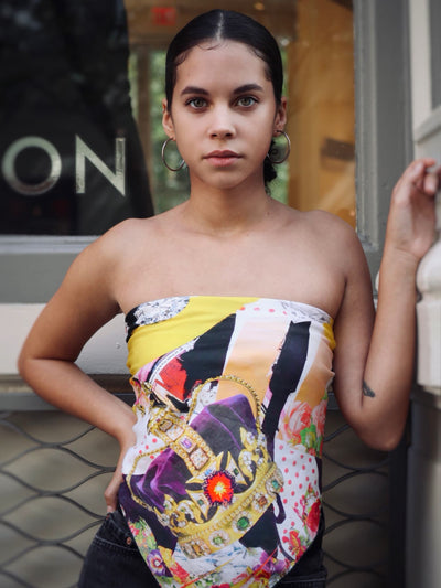 Model in the Salute to Youth 90 silk scarf by Cult Luxury, showcasing the crown motif and bold colors, paired with hoop earrings, standing by a storefront in a city setting.