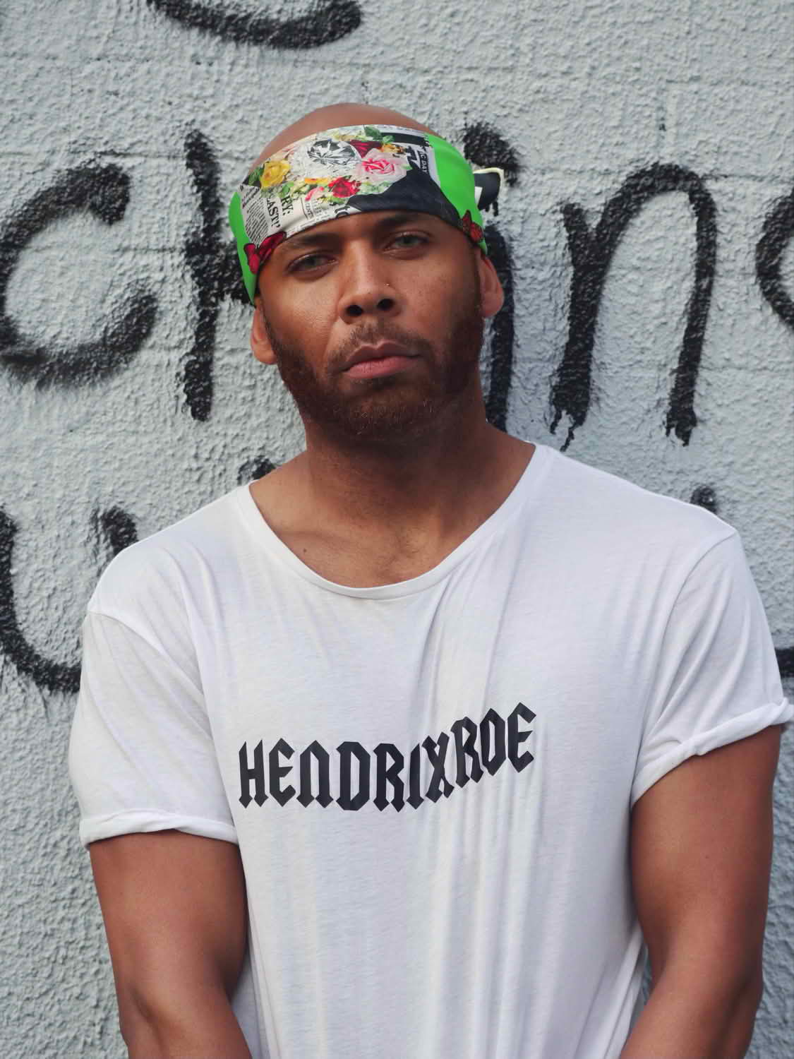 Man wearing Butterfly Season 2 luxury silk scarf styled as a headband against a graffiti wall background.