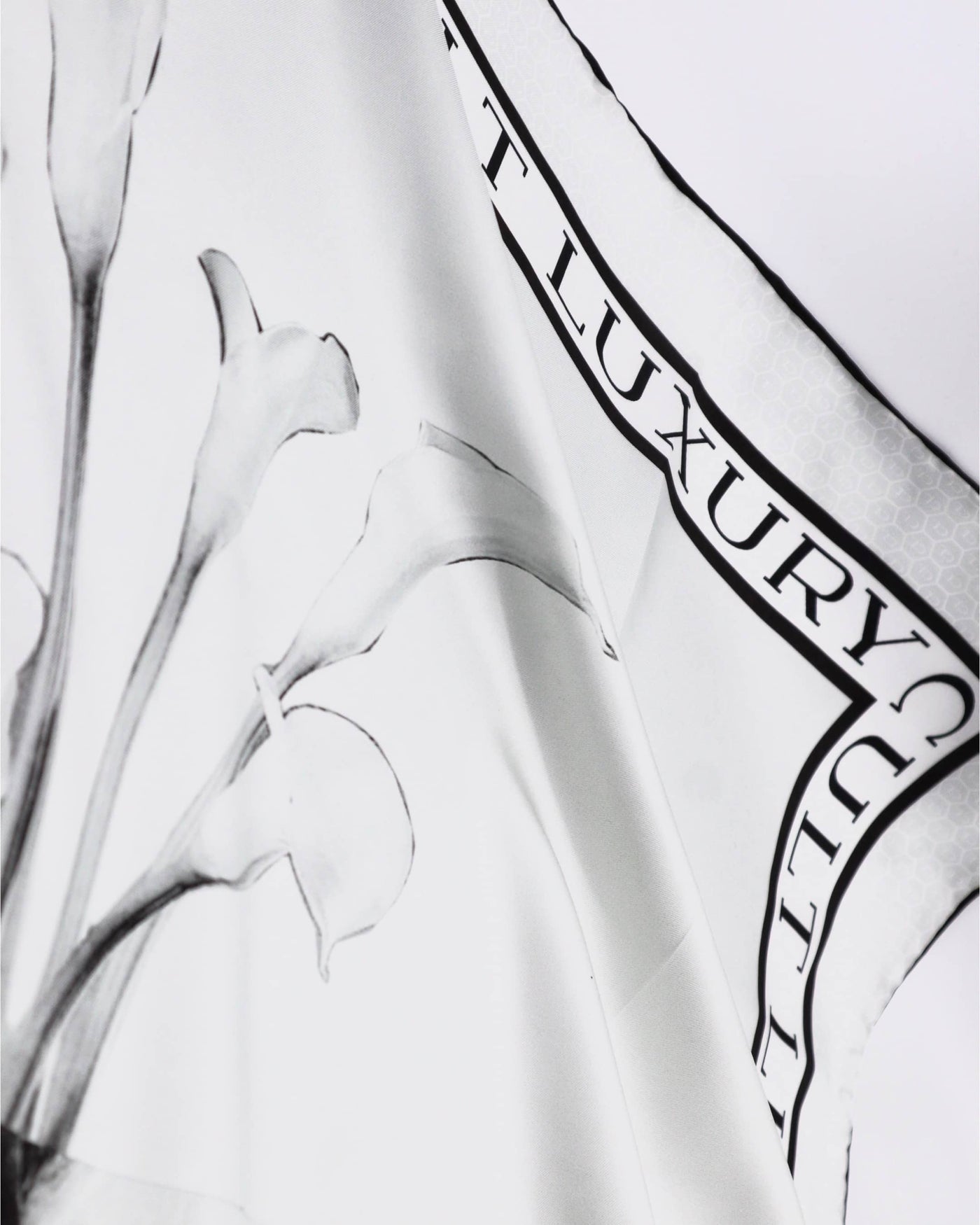 Detailed shot of the White Lily 90 scarf’s monogram border, featuring Cult Luxury’s signature white-on-white pattern on high-quality silk